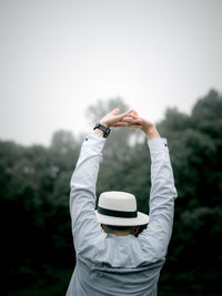 Rear view of woman with arms raised standing against sky