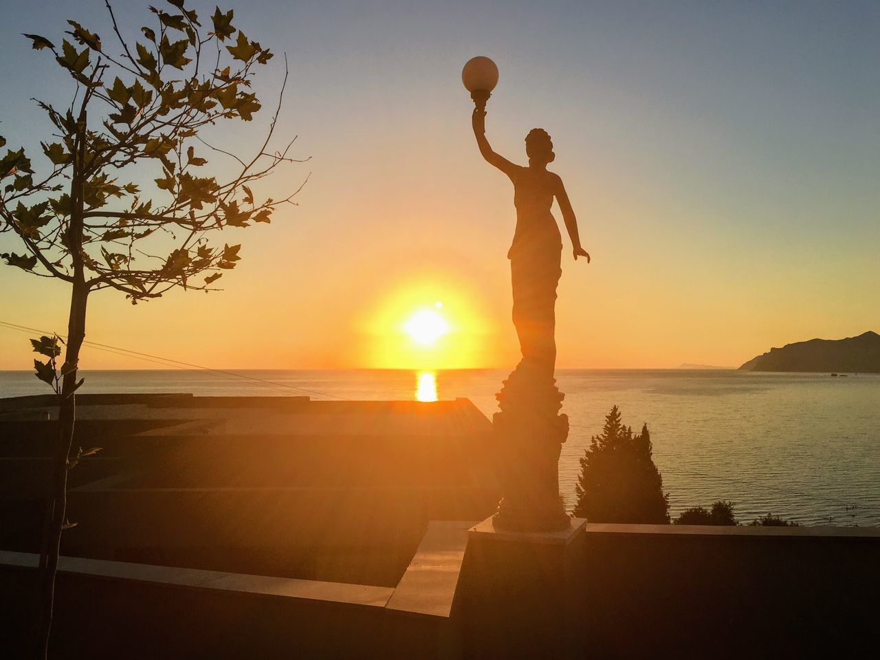 sunset, silhouette, beauty in nature, nature, leisure activity, sun, sea, sky, outdoors, real people, scenics, one person, standing, sunlight, tranquil scene, tree, beach, lifestyles, water, horizon over water, men, young adult, day