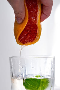 Close-up of hand squeezing grapefruit in glass over white background