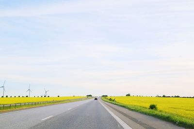 Empty road amidst field against sky