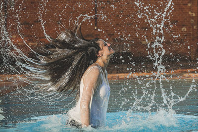 Full length of young woman splashing water 