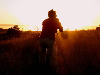 Rear view of man photographing on field against sky during sunset