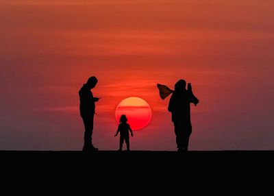 Silhouette people against orange sky during sunset