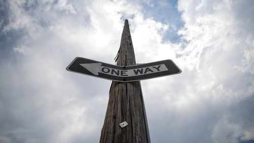 Low angle view of information sign on wooden post against sky