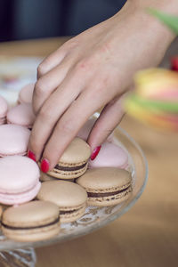 Close-up of woman hand holding macaroon in plate 