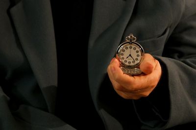 Midsection of man wearing suit holding pocket watch