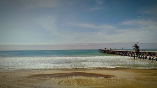 Pier at beach against cloudy sky on sunny day