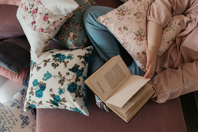 Low section of woman reading book sitting on sofa at home