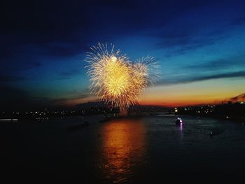 Firework display over river in city against sky