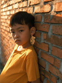 Portrait of boy standing against brick wall outdoors