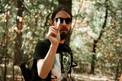 Portrait of man holding feather against trees