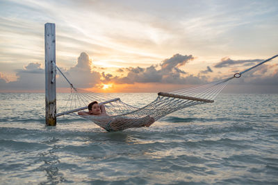 Relaxed kid on a hammock over the ocean at sunset