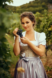 Portrait of smiling young woman holding grapes at vineyard