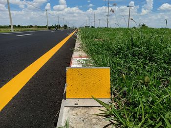 Surface level of yellow road amidst field against sky