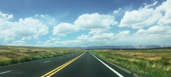 Empty road amidst field against cloudy sky