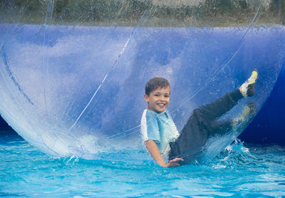 Portrait of smiling boy in large inflatable ball on swimming pool