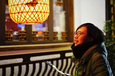 Smiling woman looking at illuminated lantern against window