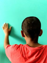 Rear view of teenage boy touching turquoise wall