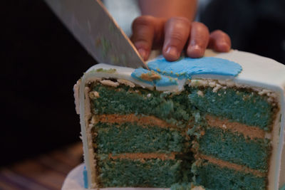 Cropped hand of person cutting cake from knife