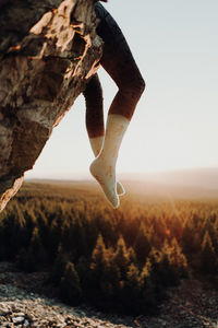 Low section of woman sitting on cliff against clear sky
