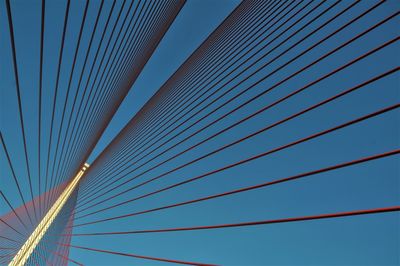 Low angle view of suspension bridge cables against blue sky