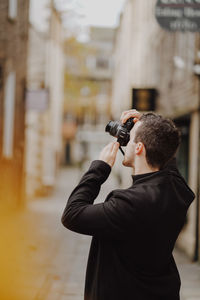 Rear view of man photographing while standing outdoors