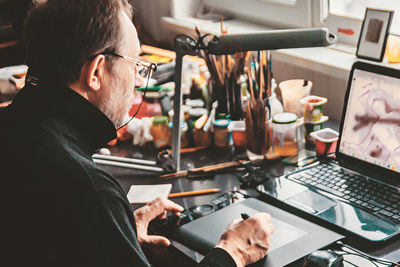 Side view of senior man using laptop and graphic tablet on desk