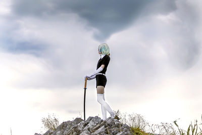 Low angle view of person standing on rock against sky