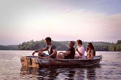 People sitting on boat in lake against sky during sunset