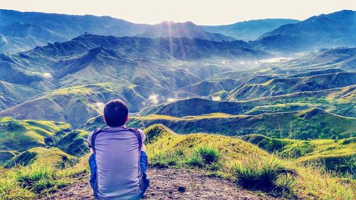 Rear view of man sitting on field against mountains