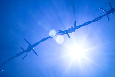 Low angle view of barbed wire against blue sky on sunny day