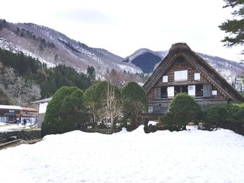 Houses on snow covered field by mountains against sky