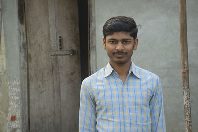 Portrait of teenage boy of indian village standing in front of the house doorway