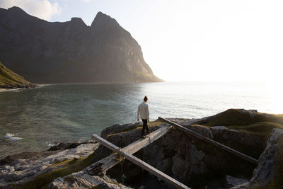 Rear view of man standing on rock by sea against sky