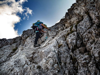 Low angle view of person climbing on rock against sky