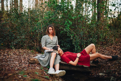 Full length of young women lying and sitting in forest