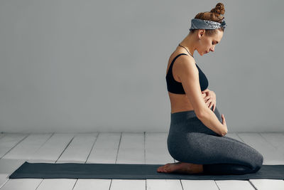 Side view of young woman sitting against wall