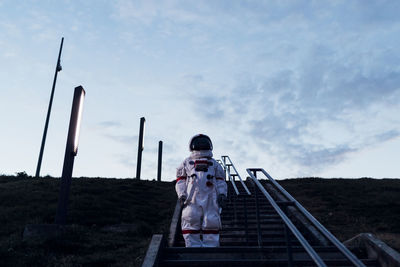 Rear view of man walking on footbridge against sky