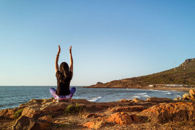 Rear view of woman on rock at beach against clear sky