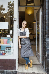 Portrait of happy female owner leaning on store doorway