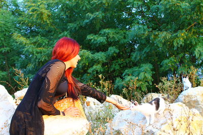 Side view of young woman petting cat on rock at park