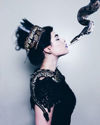 Side view of young woman with snake standing by wall