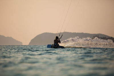 Rear view of man kitesurfing on sea against clear sky at sunset