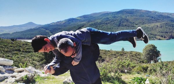 Mature man lifting grandson against river and mountains