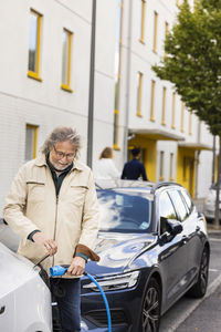 Senior man charging electric car outdoors