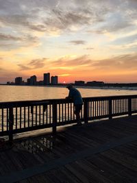 Rear view of man standing by sea against sky during sunset