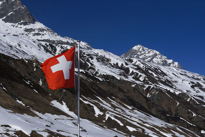 Scenic view of swiss flag in front of snowcapped mountains against clear sky