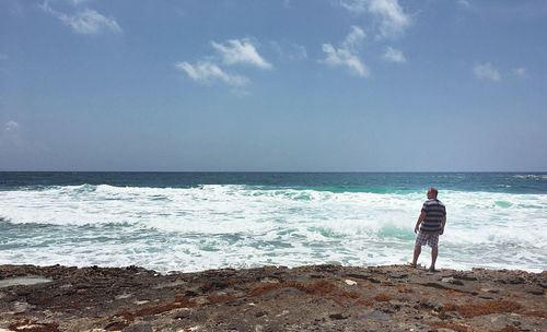 Rear view of man standing at beach against sky