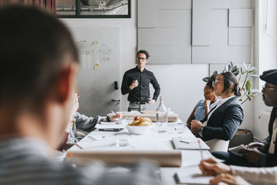 Businessman with hand on hip discussing with colleagues during meeting at office