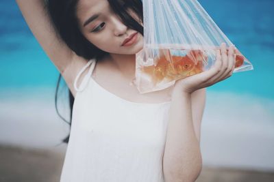 Close-up of young woman holding fish in plastic bag at beach